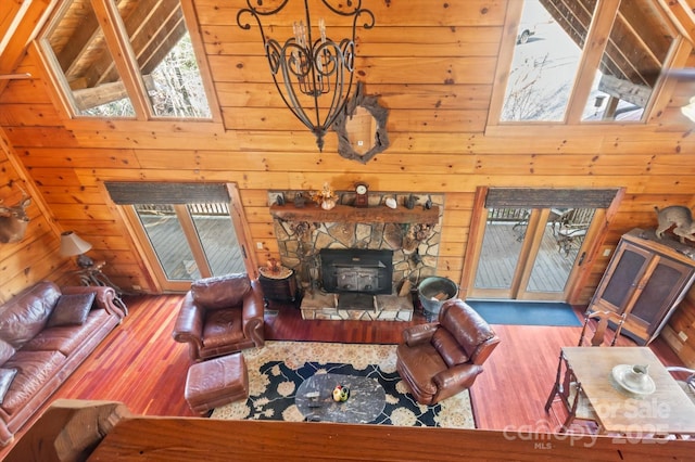 living room with hardwood / wood-style floors, high vaulted ceiling, a stone fireplace, and wooden walls