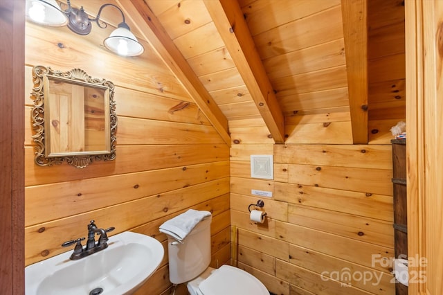 bathroom featuring wood walls, lofted ceiling with beams, sink, toilet, and wood ceiling