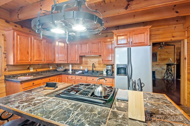 kitchen featuring ceiling fan, sink, refrigerator with ice dispenser, stainless steel gas stovetop, and wood walls