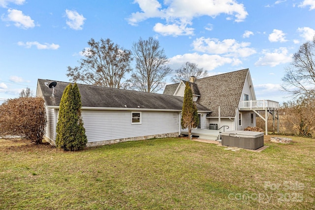 back of property featuring a lawn, a wooden deck, and a hot tub