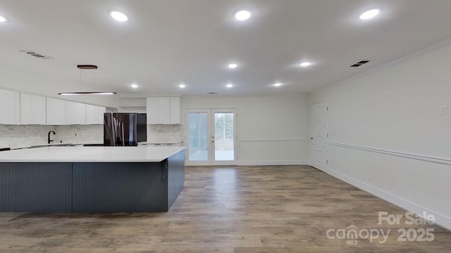 kitchen with white cabinetry, sink, ornamental molding, stainless steel fridge, and light wood-type flooring