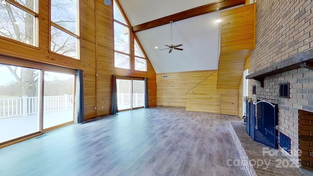 unfurnished living room with a brick fireplace, ceiling fan, wooden walls, hardwood / wood-style flooring, and high vaulted ceiling