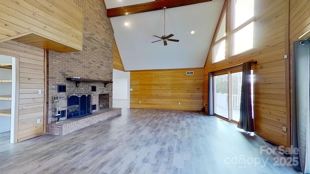 unfurnished living room featuring ceiling fan, a brick fireplace, high vaulted ceiling, wood walls, and hardwood / wood-style flooring