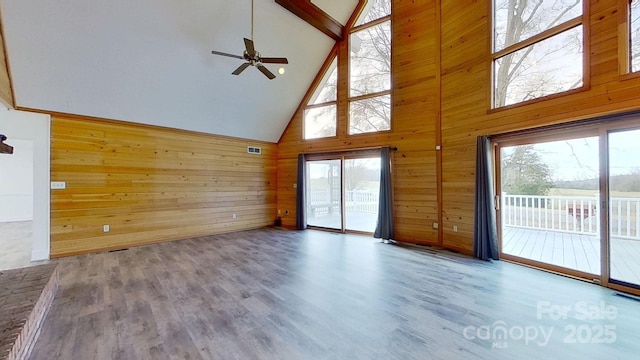 unfurnished living room featuring wood walls, high vaulted ceiling, hardwood / wood-style flooring, ceiling fan, and beamed ceiling