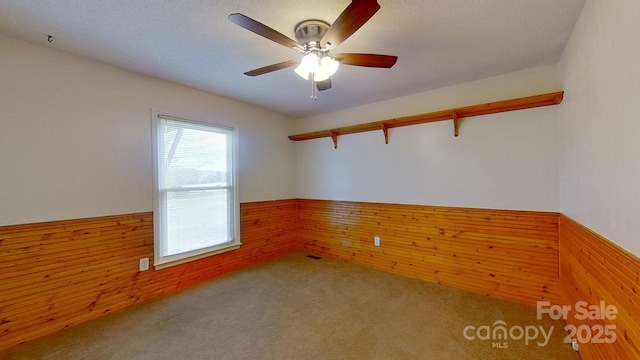 carpeted spare room with ceiling fan and wood walls