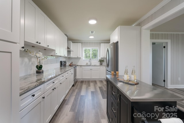 kitchen with white cabinets, sink, light hardwood / wood-style flooring, ornamental molding, and stainless steel appliances