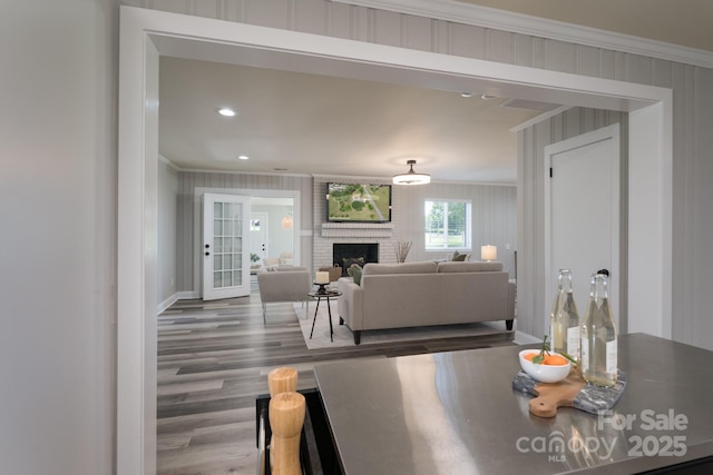 dining area featuring wood-type flooring, ornamental molding, wooden walls, and a brick fireplace