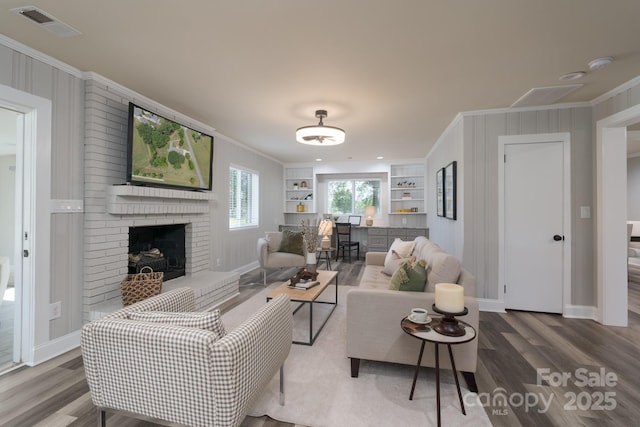 living room featuring crown molding, built in features, hardwood / wood-style flooring, and a brick fireplace