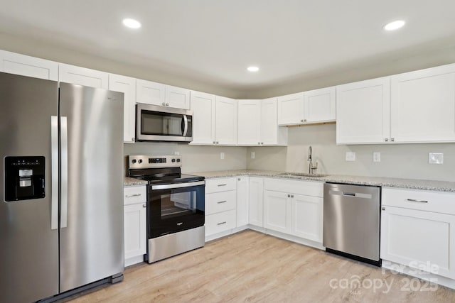 kitchen featuring light stone countertops, stainless steel appliances, sink, light hardwood / wood-style flooring, and white cabinets