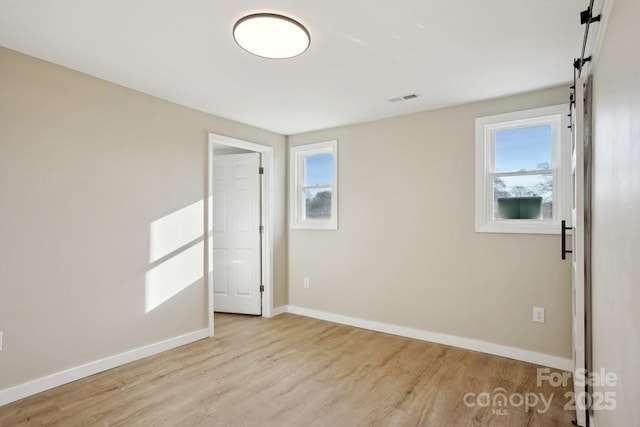 unfurnished room with a barn door, light hardwood / wood-style flooring, and a healthy amount of sunlight