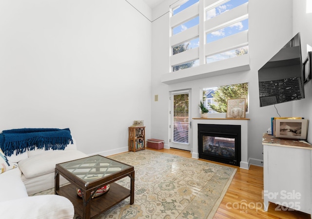 living room featuring a multi sided fireplace, a towering ceiling, and light hardwood / wood-style floors