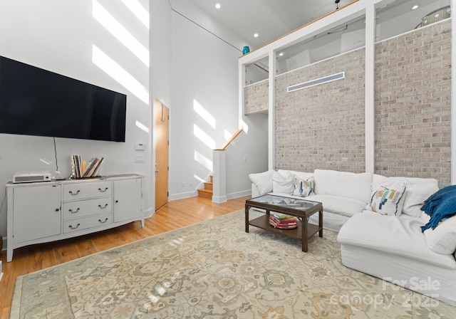 living room with light hardwood / wood-style flooring, a towering ceiling, and brick wall