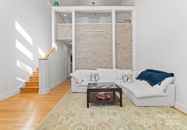 living room with a towering ceiling, hardwood / wood-style flooring, and brick wall