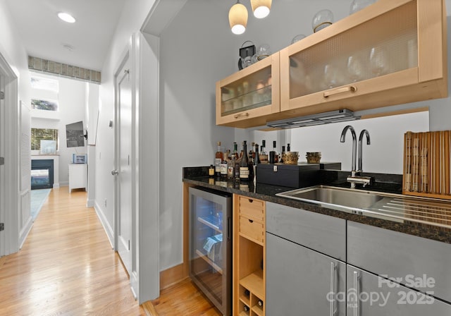 bar with light wood-type flooring, sink, beverage cooler, and dark stone counters