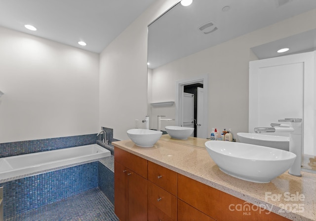 bathroom with tile patterned floors, vanity, and a relaxing tiled tub