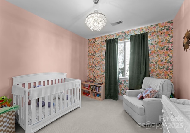 bedroom with a crib, carpet floors, and a chandelier