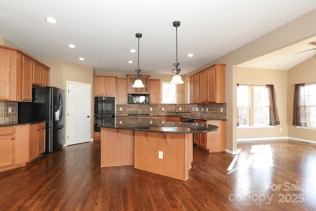 kitchen featuring dark stone counters, black appliances, hanging light fixtures, a kitchen island, and dark hardwood / wood-style flooring