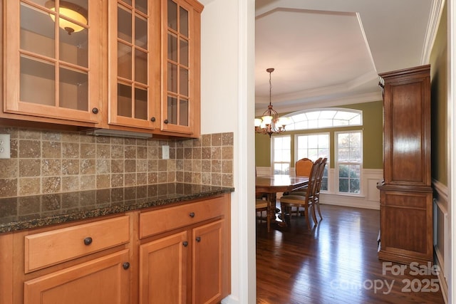 kitchen featuring ornamental molding, dark stone counters, dark wood-type flooring, a chandelier, and hanging light fixtures