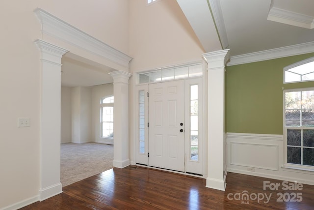 entryway featuring dark colored carpet, ornate columns, and crown molding