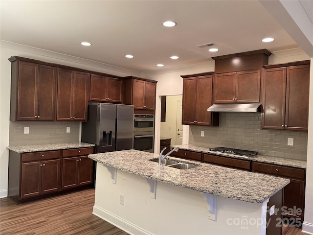 kitchen with appliances with stainless steel finishes, an island with sink, sink, a kitchen breakfast bar, and light stone countertops