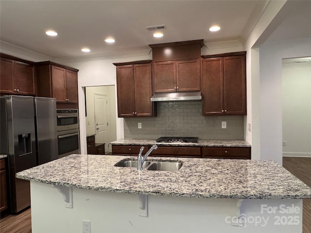 kitchen with appliances with stainless steel finishes, sink, a kitchen island with sink, and a kitchen bar