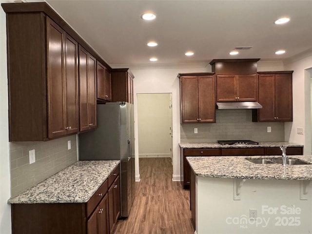 kitchen featuring dark brown cabinetry, sink, a breakfast bar area, light wood-type flooring, and light stone countertops