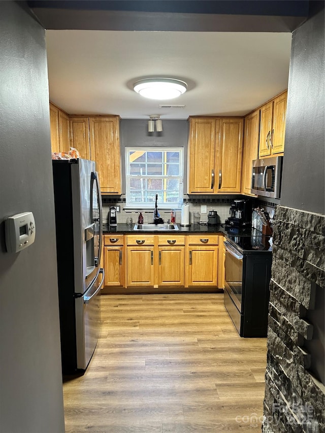 kitchen with a sink, light wood-type flooring, dark countertops, and appliances with stainless steel finishes