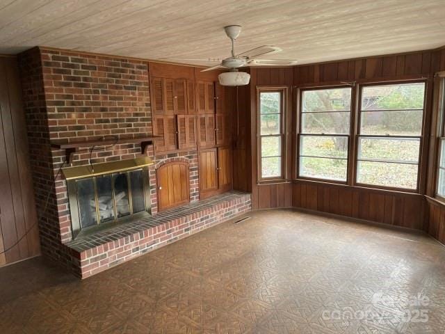 unfurnished living room featuring wood walls, a fireplace, ceiling fan, and wood ceiling