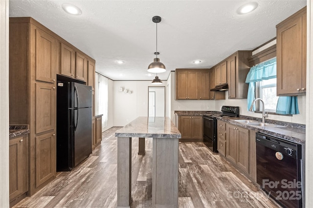 kitchen with brown cabinetry, pendant lighting, a sink, and black appliances