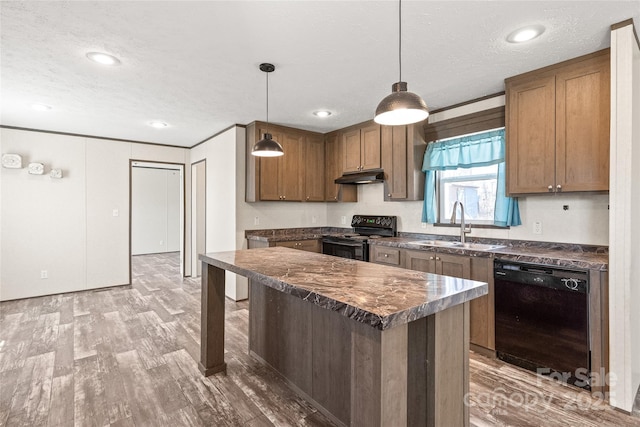 kitchen with decorative light fixtures, dark countertops, a sink, under cabinet range hood, and black appliances