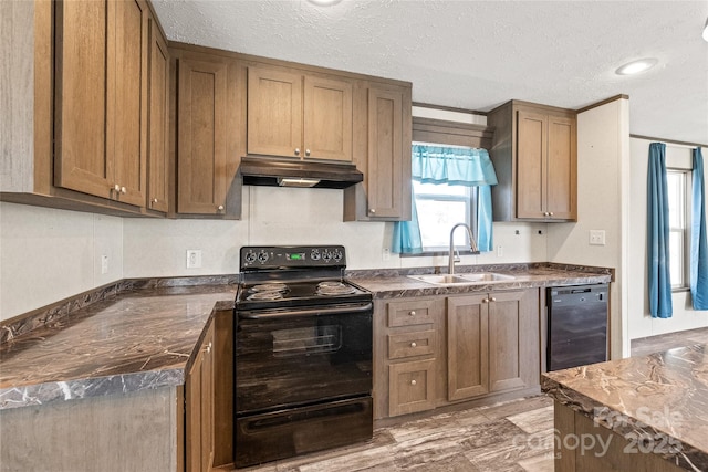 kitchen with dark countertops, brown cabinets, under cabinet range hood, black appliances, and a sink