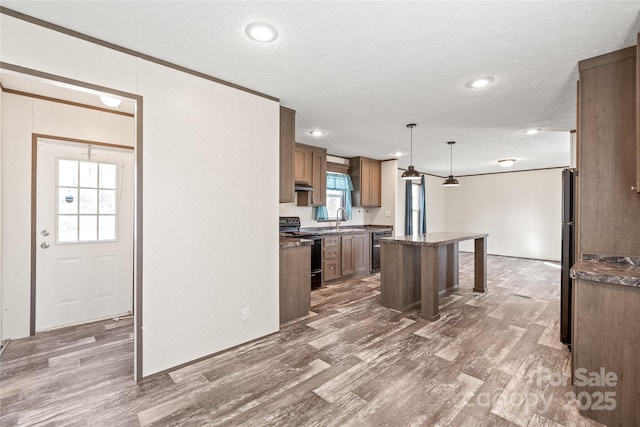 kitchen featuring a breakfast bar, a sink, hanging light fixtures, a center island, and black appliances