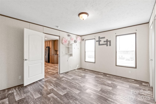 empty room featuring a textured ceiling, wood finished floors, and crown molding