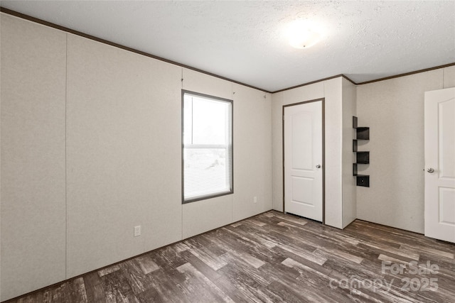 empty room with a textured ceiling, ornamental molding, and dark wood-style flooring