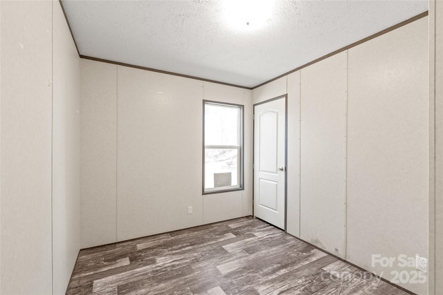 spare room with a textured ceiling, wood finished floors, and crown molding