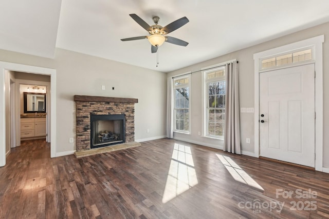 unfurnished living room featuring ceiling fan, dark wood-type flooring, and a stone fireplace