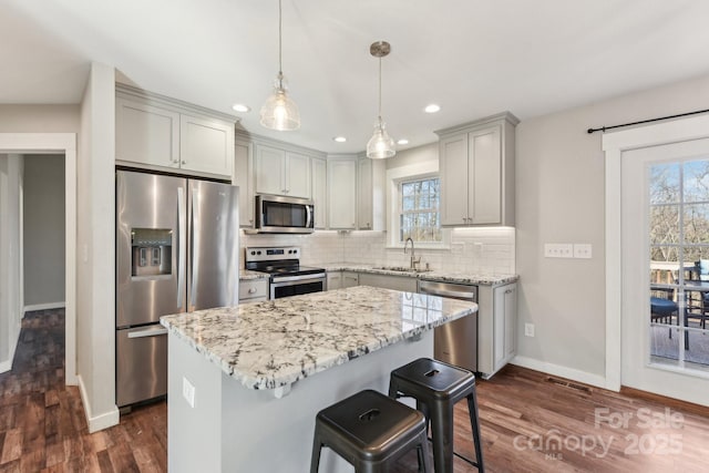 kitchen with appliances with stainless steel finishes, decorative light fixtures, sink, light stone countertops, and a center island