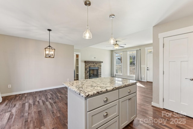 kitchen featuring a center island, decorative light fixtures, a stone fireplace, ceiling fan, and light stone counters