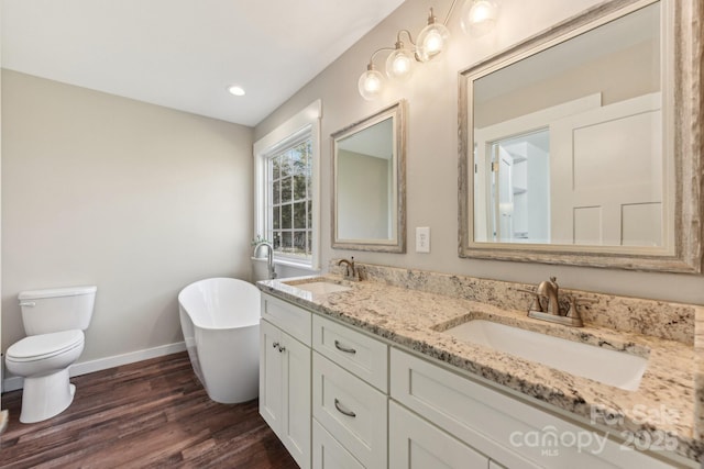 bathroom featuring a washtub, wood-type flooring, toilet, and vanity