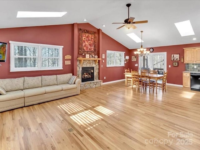 living room with ceiling fan with notable chandelier, light hardwood / wood-style floors, a stone fireplace, and lofted ceiling