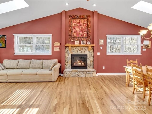 living room with a chandelier, wood-type flooring, a stone fireplace, and vaulted ceiling with skylight