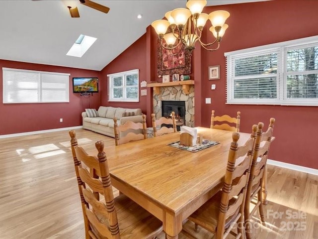 dining space with lofted ceiling with skylight, a fireplace, ceiling fan with notable chandelier, and light wood-type flooring