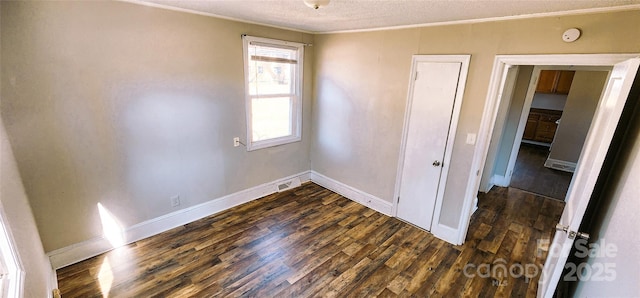 empty room with a textured ceiling, ornamental molding, and dark hardwood / wood-style flooring