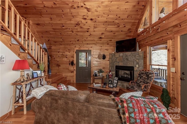 living room with wood walls, a stone fireplace, light wood-type flooring, and wooden ceiling