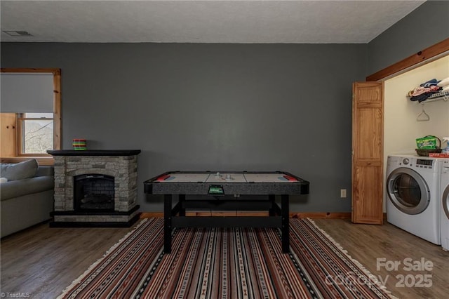 recreation room with hardwood / wood-style floors, a stone fireplace, and washing machine and clothes dryer