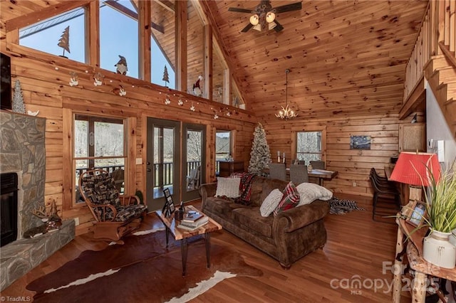 unfurnished living room with hardwood / wood-style floors, ceiling fan with notable chandelier, and a stone fireplace