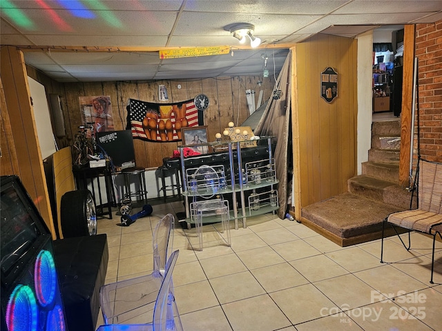 interior space featuring tile patterned floors, a drop ceiling, and wood walls