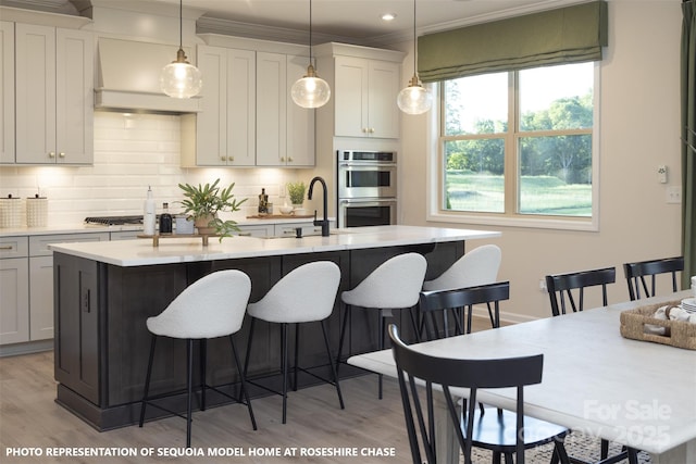 kitchen featuring sink, an island with sink, appliances with stainless steel finishes, light hardwood / wood-style floors, and a breakfast bar area