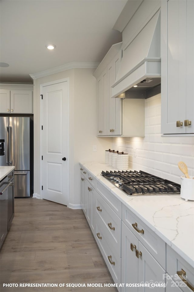 kitchen featuring white cabinetry, light stone countertops, light hardwood / wood-style flooring, custom exhaust hood, and appliances with stainless steel finishes