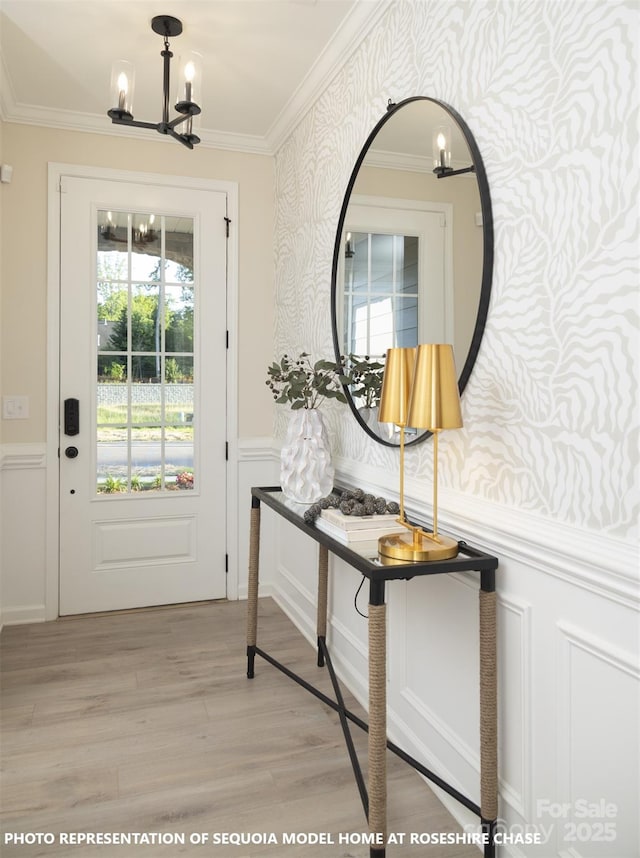 entryway with wallpapered walls, a wainscoted wall, ornamental molding, light wood-style floors, and a notable chandelier